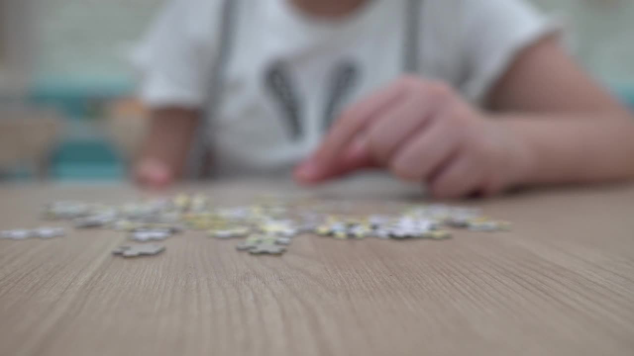 一个孩子在木桌上拼拼图。靠近手部。视频素材