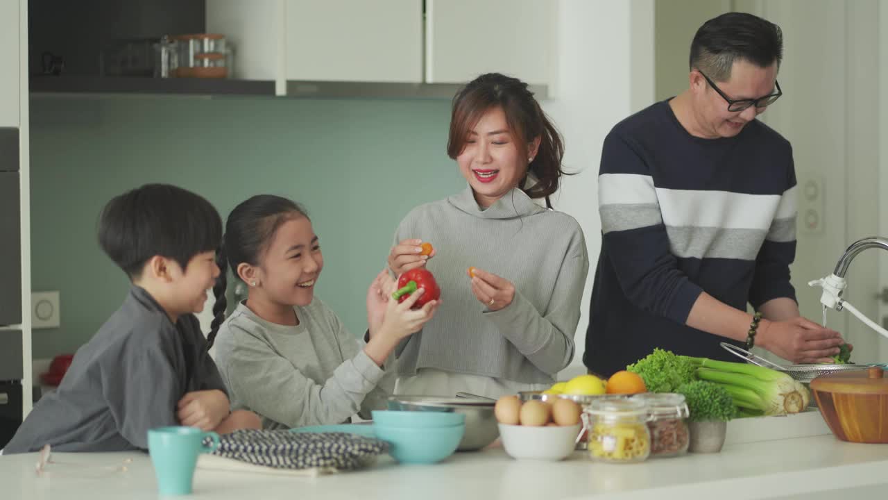 顽皮的亚洲华人家庭和两个孩子在厨房准备食物，一起享受快乐时光视频素材
