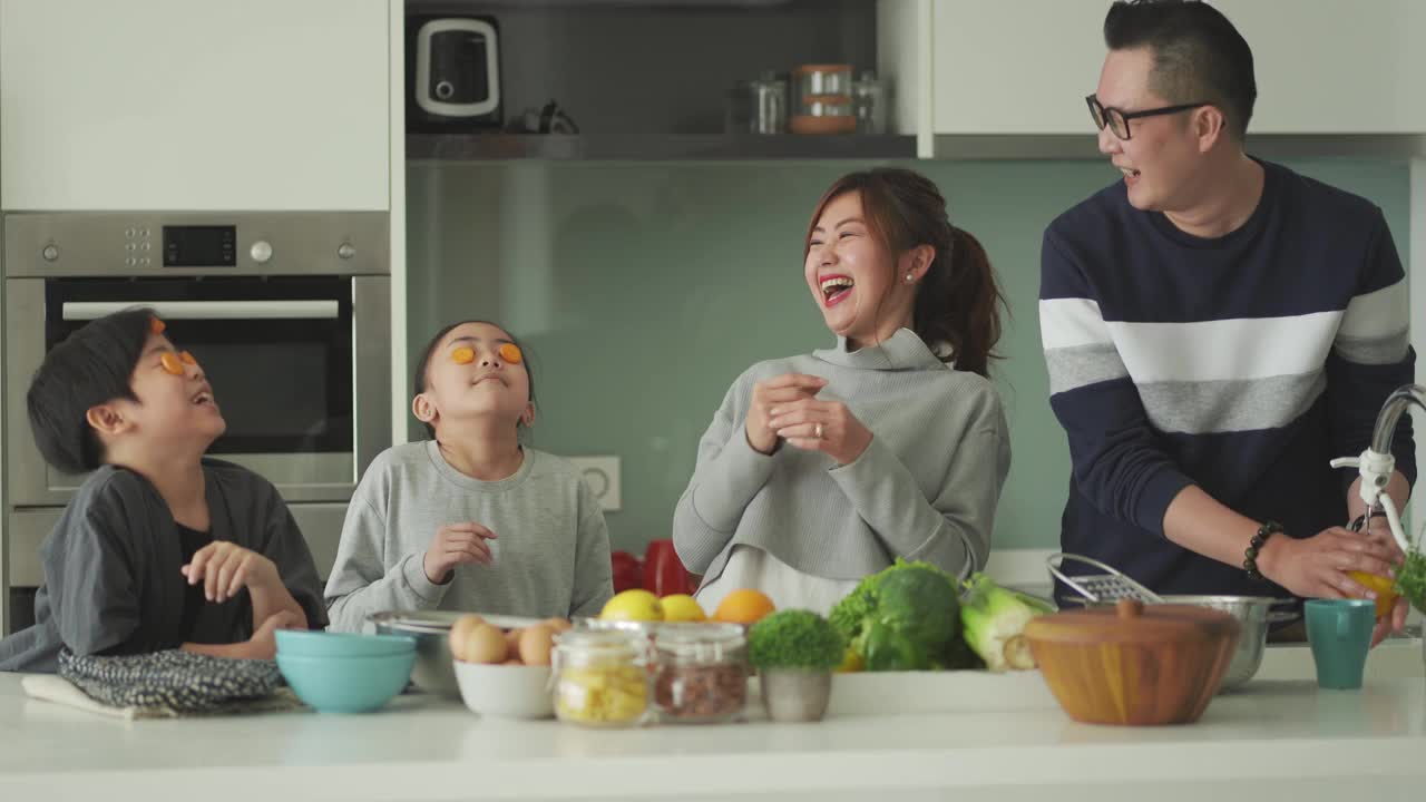 顽皮的亚洲华人家庭和两个孩子在厨房准备食物，一起享受快乐时光视频素材