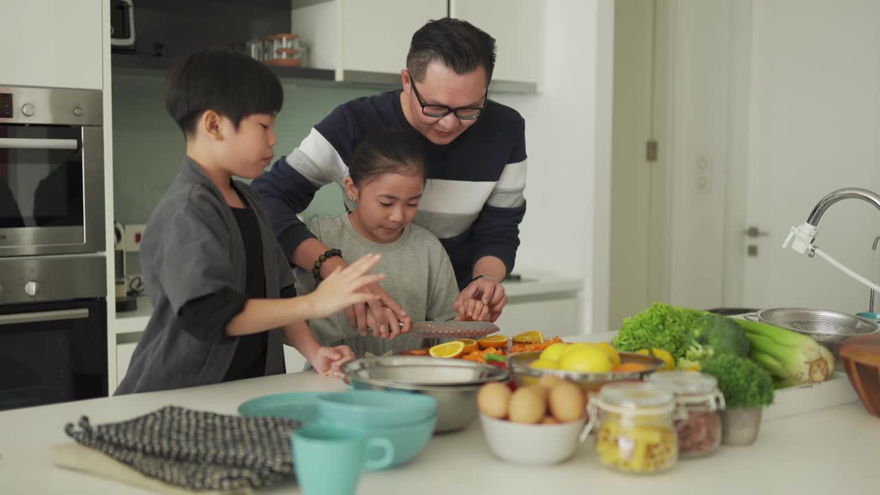 亚洲华人父女在厨房柜台边切橘子边和儿子一起吃饭视频素材