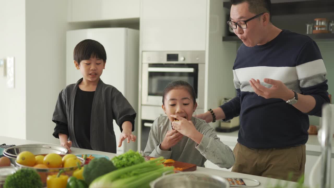 亚洲华人父女在厨房柜台边切橘子边和儿子一起吃饭视频下载