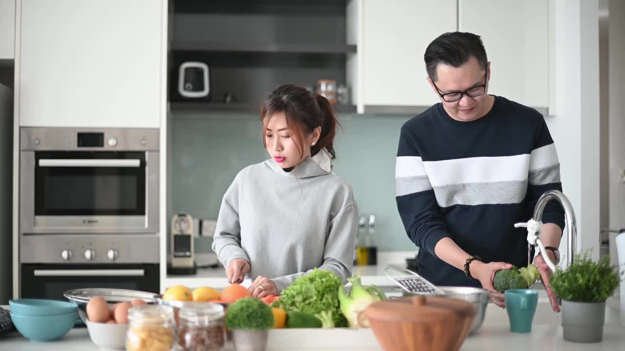 亚洲华人夫妇一起在厨房柜台准备食物，在周末聚在一起视频素材