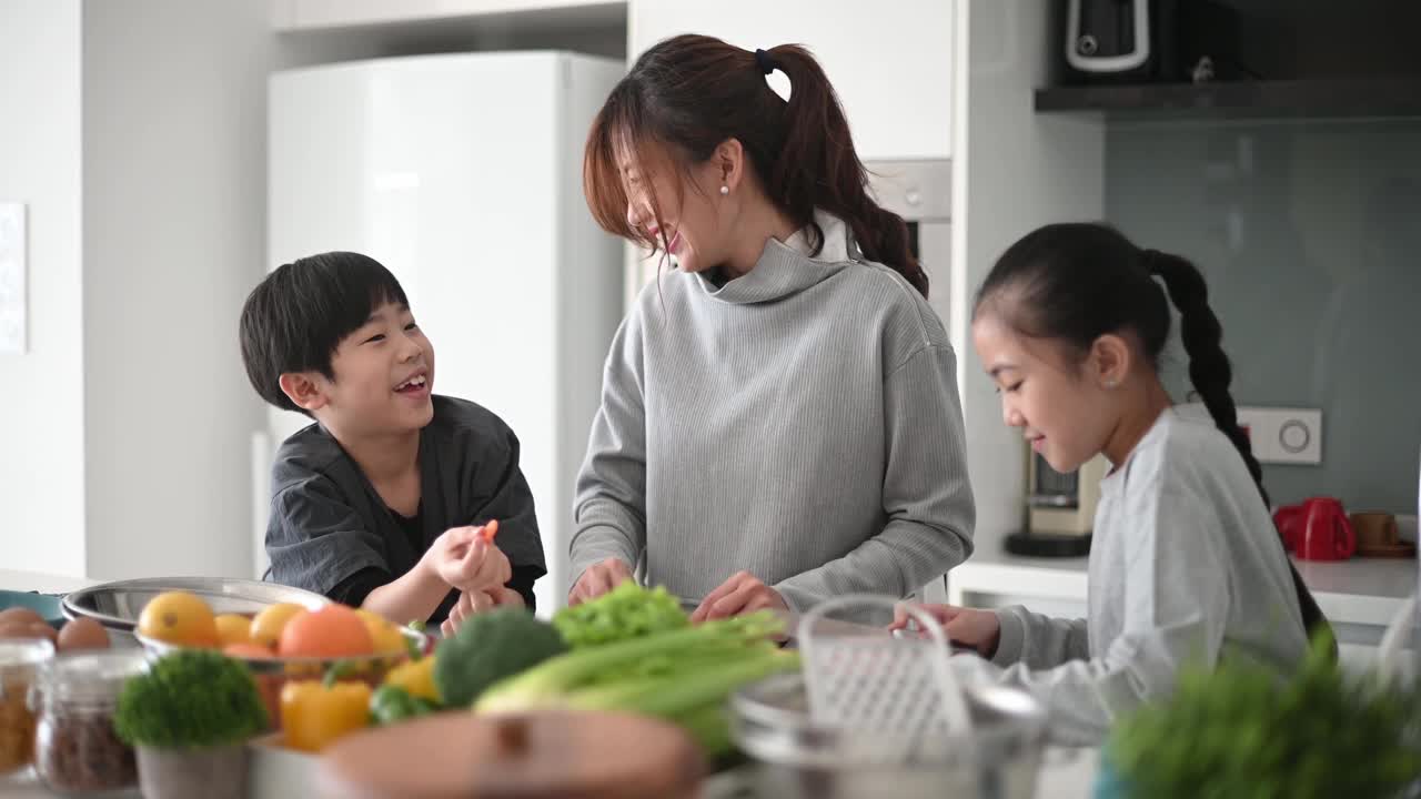 亚洲中国母亲和女儿儿子在厨房里切碎胡萝卜准备凉拌卷心菜沙拉视频素材