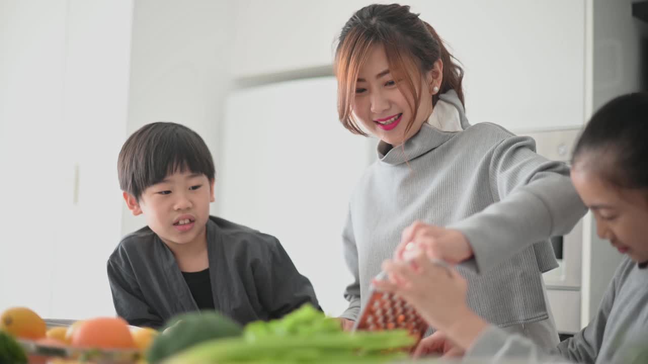 亚洲中国母亲和女儿儿子在厨房里切碎胡萝卜准备凉拌卷心菜沙拉视频下载
