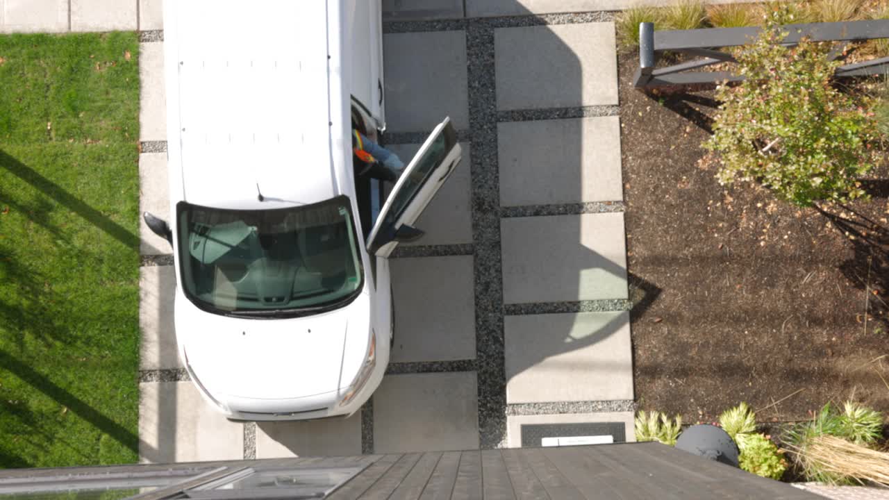 从头顶拍摄的照片中，女送货司机将一箱有机农产品从货车上取下，然后将盒子搬到家的前门视频素材