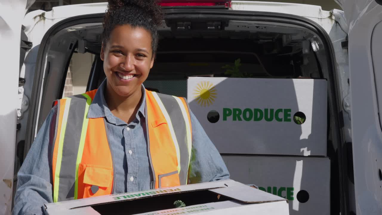 中特写镜头，微笑的女送货司机站在货车后面，手里拿着新鲜的有机农产品盒，送货到家视频素材