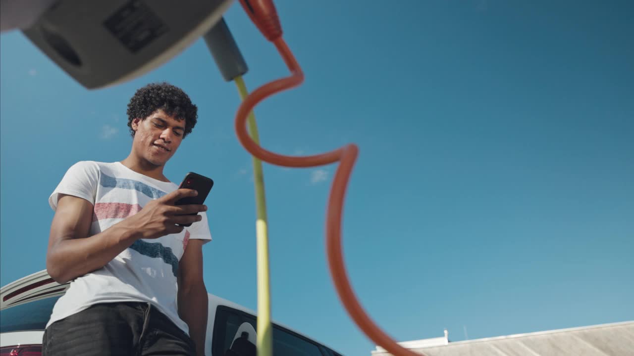 年轻男子在停车场充电时使用手机的低角度照片视频下载