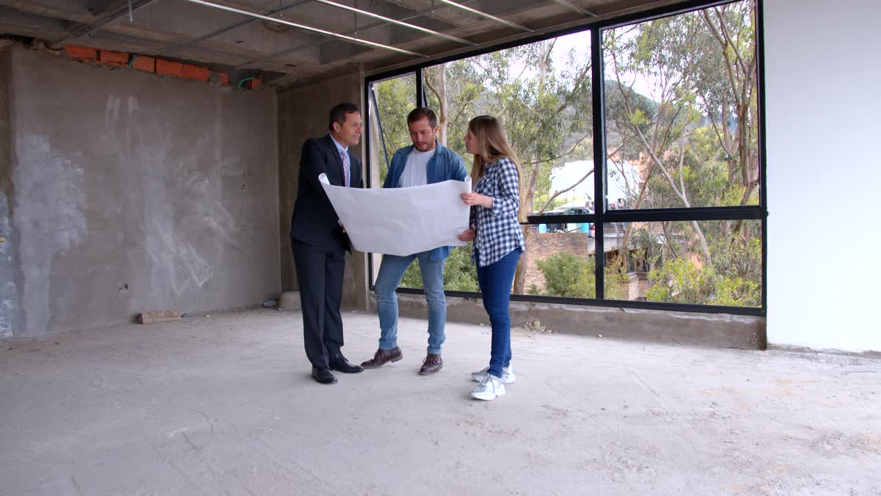 房地产开发商一边给新婚夫妇看房子的设计图，一边指着工地的不同方向视频素材