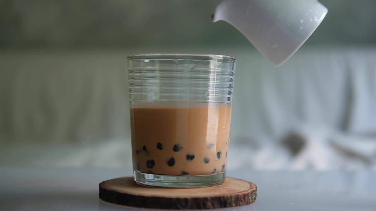 在玻璃杯中倒入加珍珠泡的泰国奶茶。慢动作视频下载