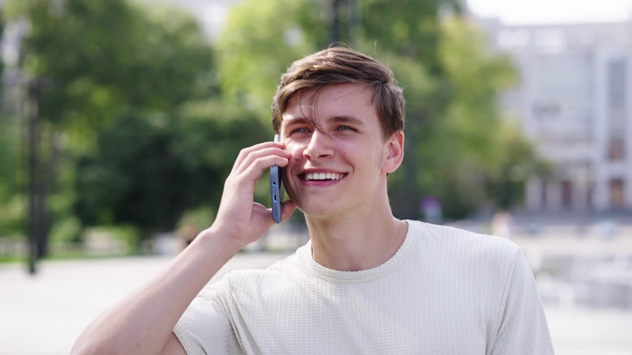 一个快乐的年轻人在城里散步时讲电话视频素材