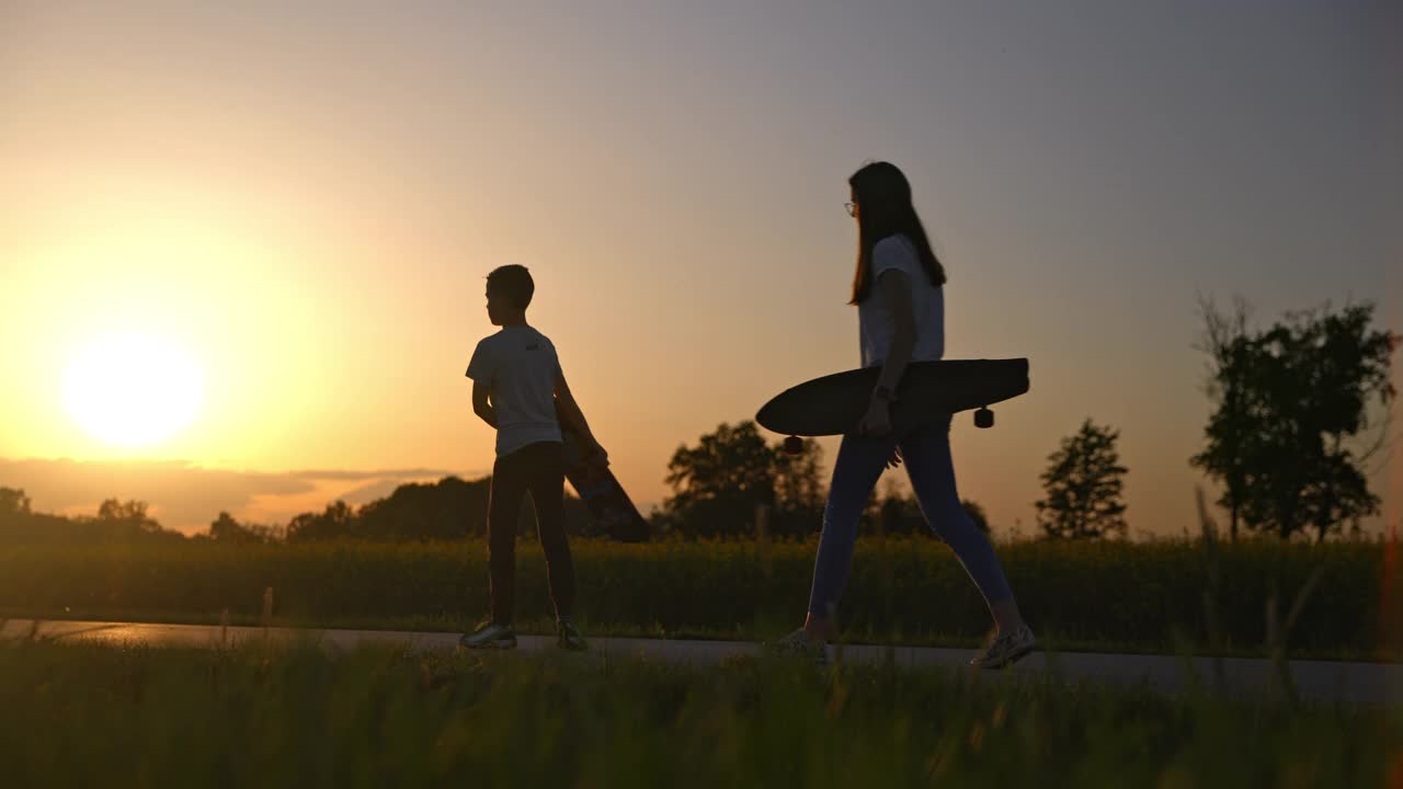 十几岁的女孩和男孩扛着滑板在农村的道路上视频素材