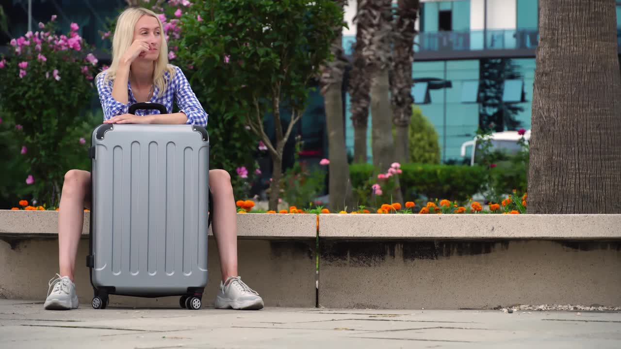 一个带着灰色行李箱的漂亮女人在机场附近等商务航班。视频下载