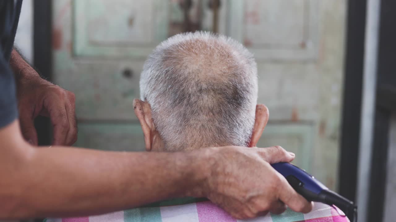 4K分辨率的父子老人在室内用理发器在家梳洗。在冠状病毒隔离期间，请呆在家里理发。自己动手，理发师。东南亚的泰国视频素材