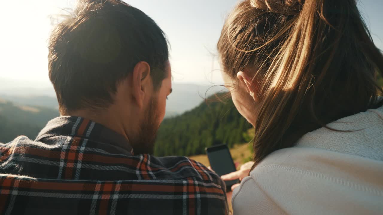 年轻夫妇在山上放松时使用智能手机。视频下载