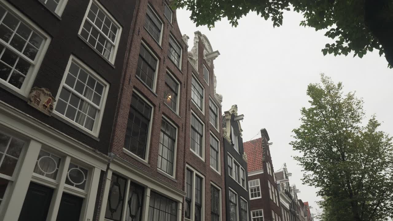 观景:沿着街道走，看到荷兰风格的房子是沿着阿姆斯特丹的一条小路在恶劣的天气，手持观看视频素材