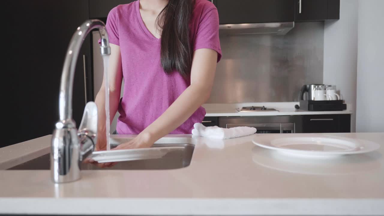 年轻女子在家里的厨房水槽里洗盘子和水果视频下载