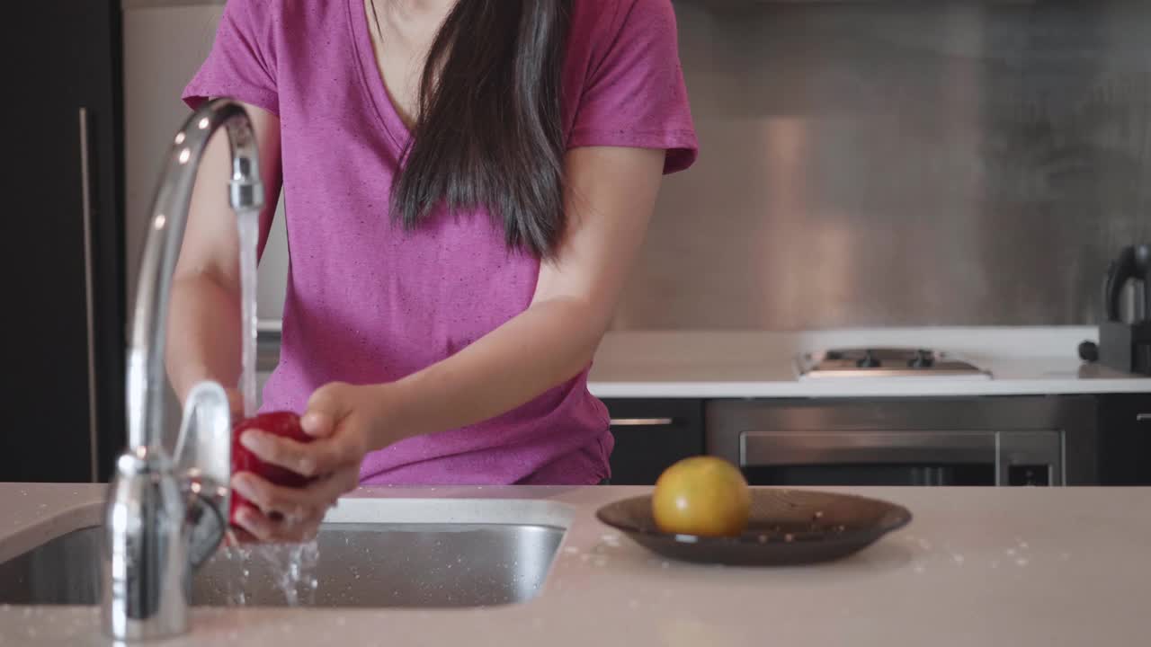 年轻女子在家里的厨房水槽里洗盘子和水果视频下载