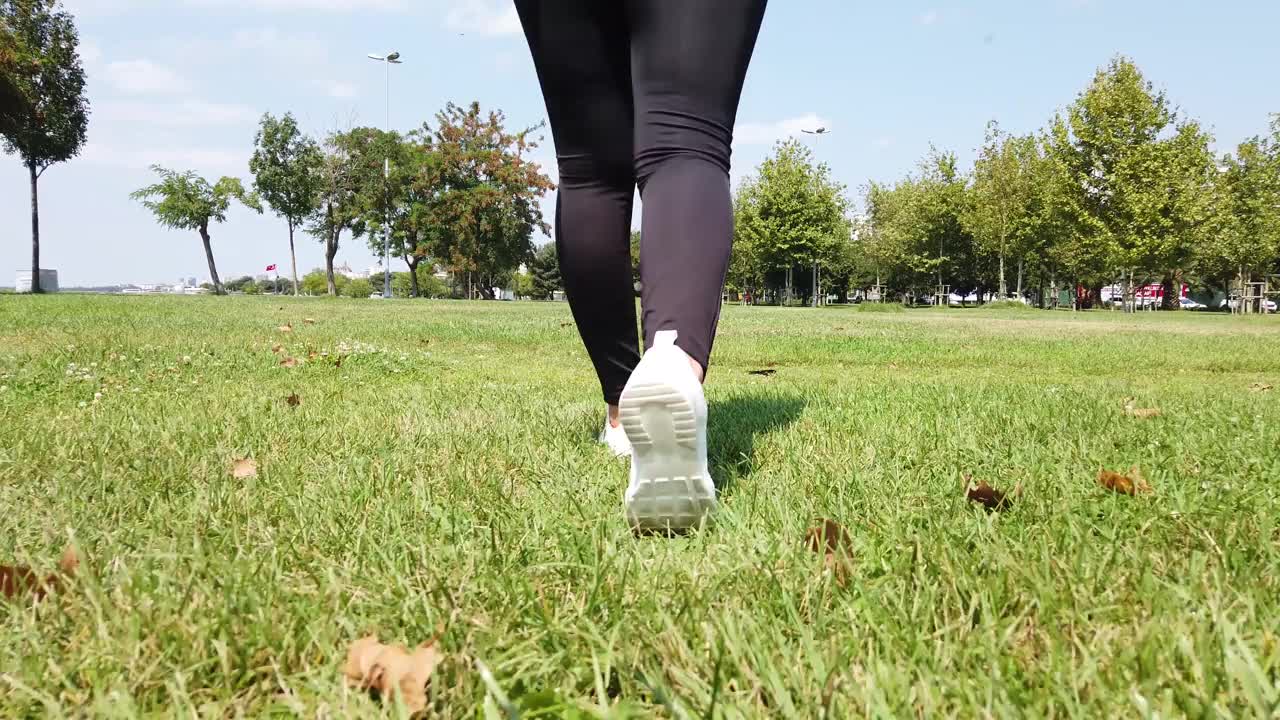 特写镜头是穿着白色运动鞋在草地上行走的女性腿视频下载
