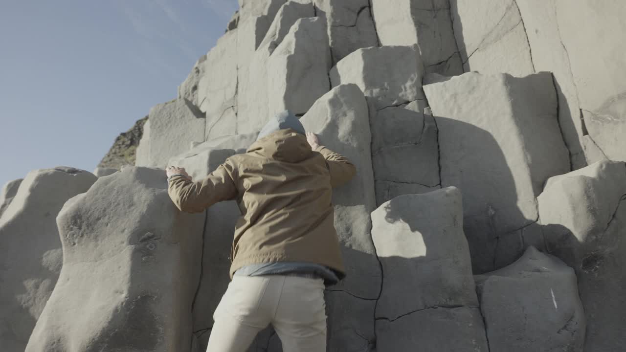 男子攀登玄武岩柱的低角度视图/维克，冰岛视频下载