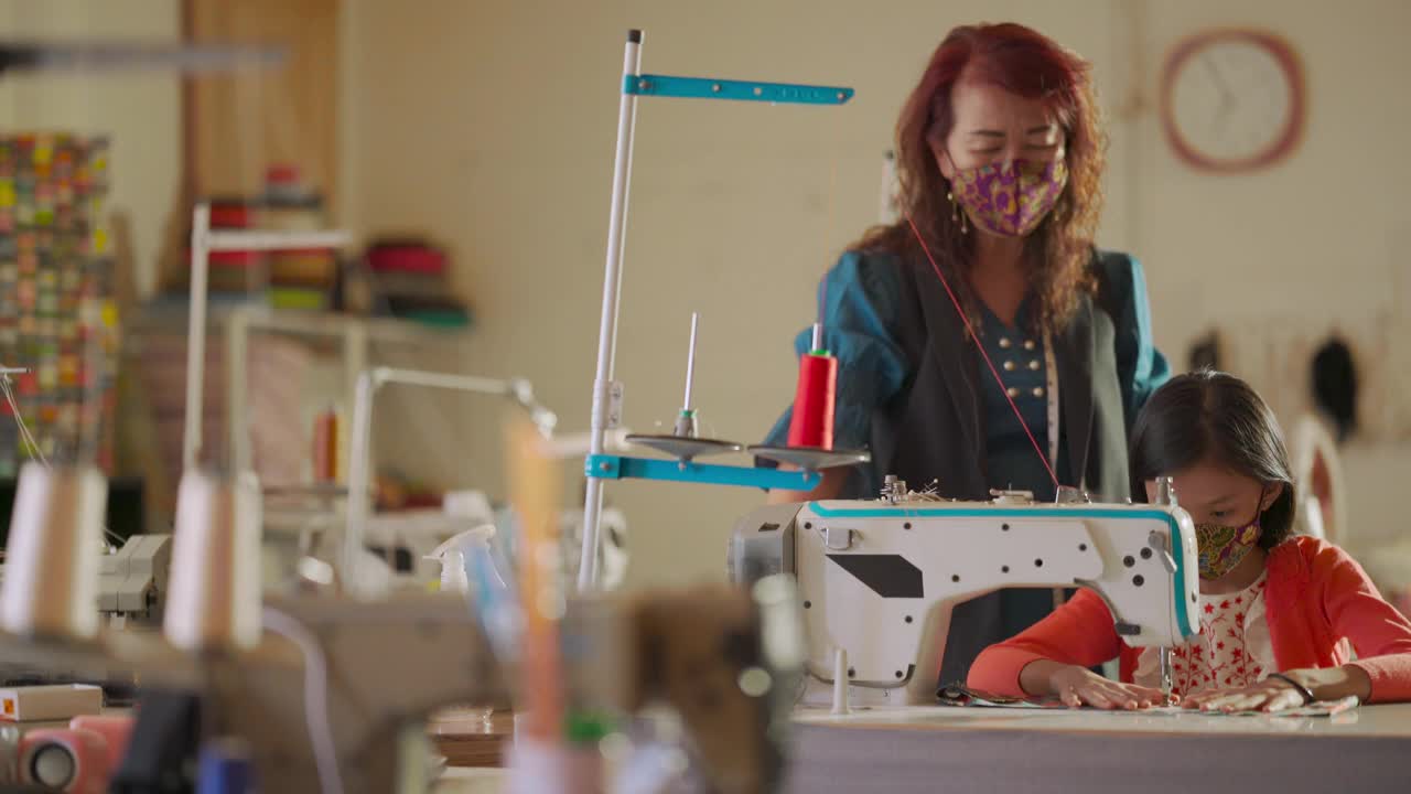 亚裔华裔女教师在工作室教育课上指导年轻女学生用缝纫机缝制蜡染布防护口罩视频素材