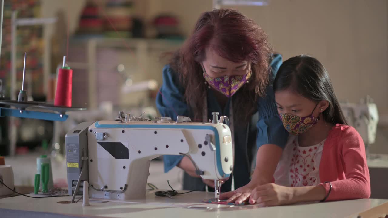 亚裔华裔女教师在工作室教育课上指导年轻女学生用缝纫机缝制蜡染布防护口罩视频素材