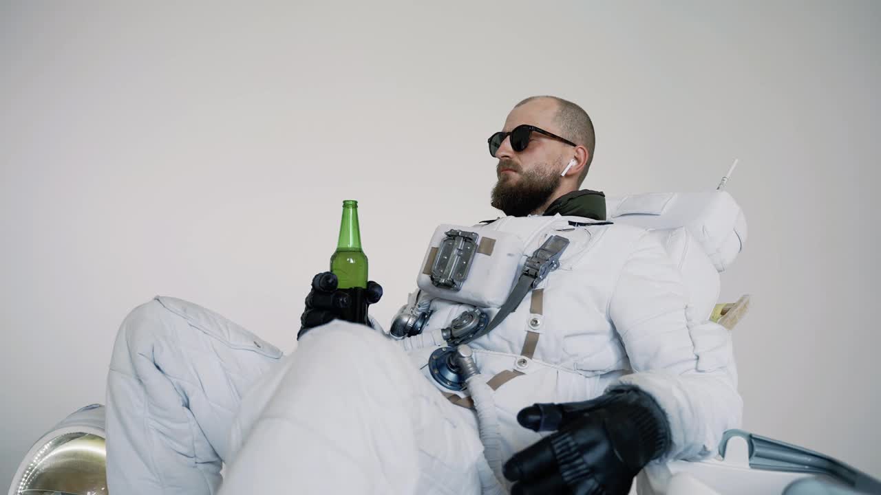 宇航员坐在椅子上，手里拿着瓶子喝着。工作室视频素材