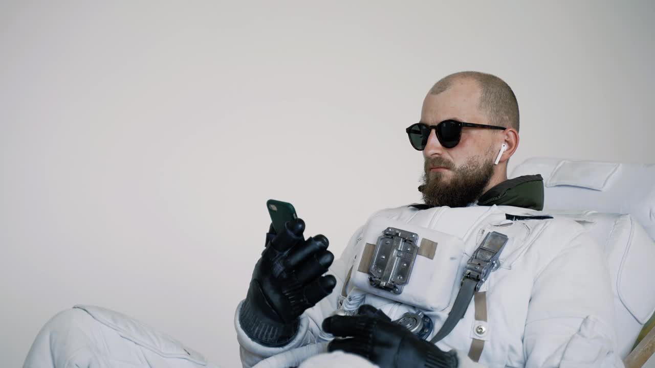 宇航员坐在椅子上，手里拿着电话，听着音乐。工作室视频下载