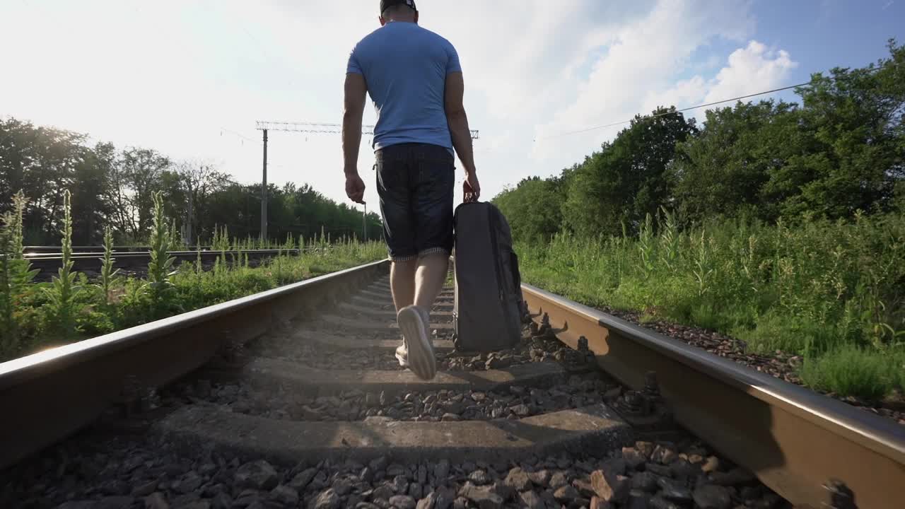 心烦意乱的男人穿着短裤沿着铁路走，拿着公路包视频下载