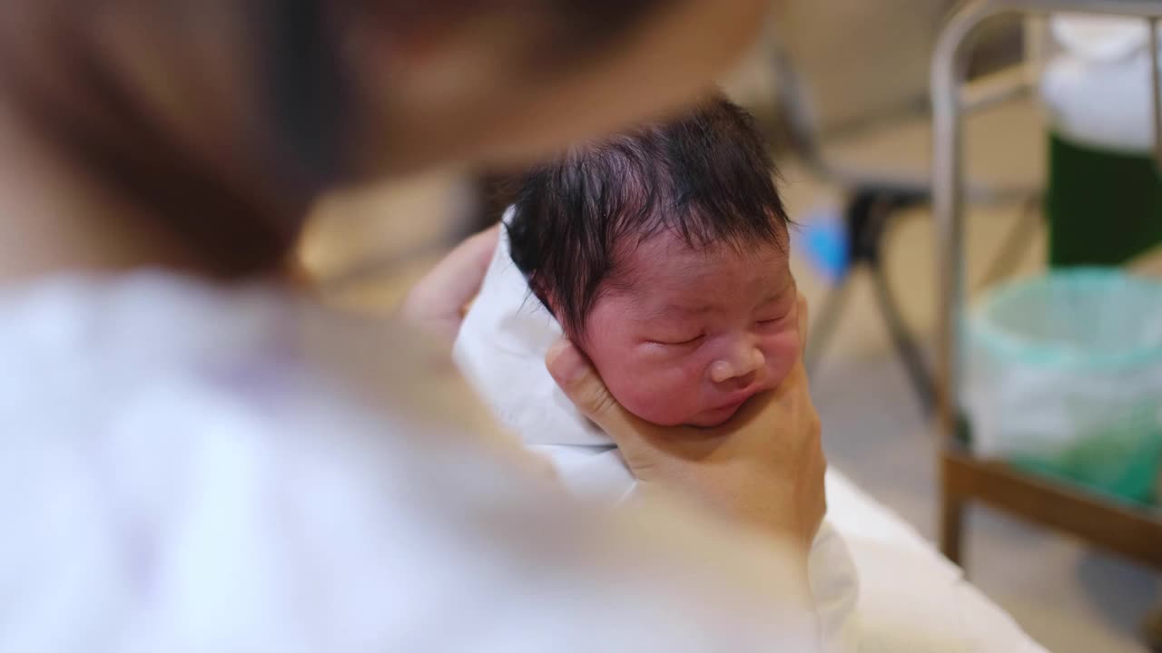 一名亚裔妇女在医院里抱着她刚出生的男婴。在这里，她斜倚着，抱着孩子靠近她的胸部安慰他。视频下载