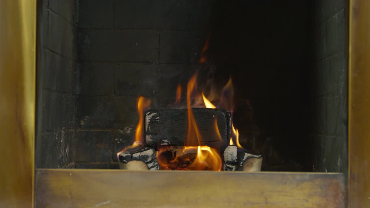 那人拖着一根黑铁拨火棍在壁炉里生火。从房子里的耐火砖上烧木柴到石头壁炉里视频素材