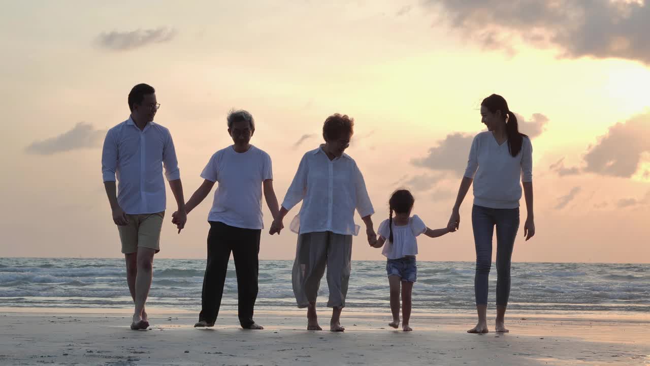 剪影中，快乐的亚洲大家庭五人手牵着手，走向日落海边的沙滩冲浪。幸福在自然的概念。视频素材