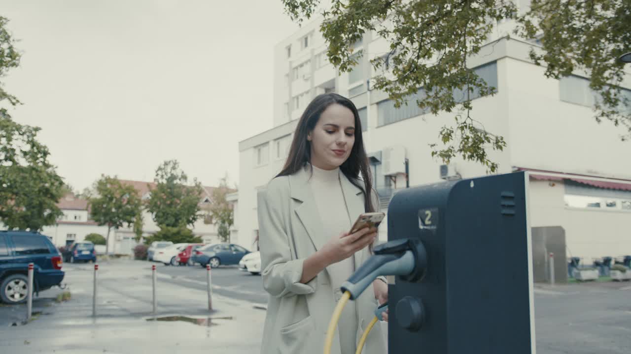 一名女子在电动汽车充电站为她的电动汽车充电时进行移动支付视频素材