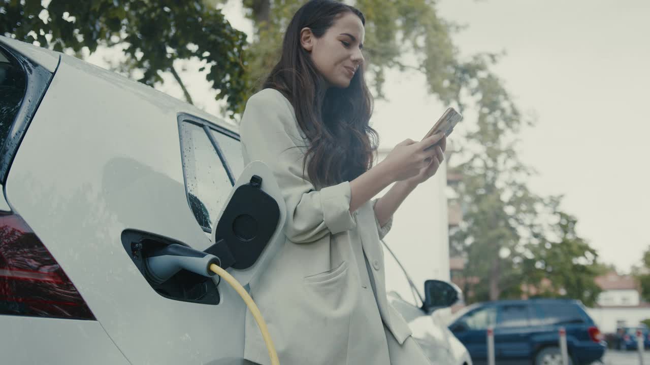 一名女子在电动汽车充电时视频通话视频素材