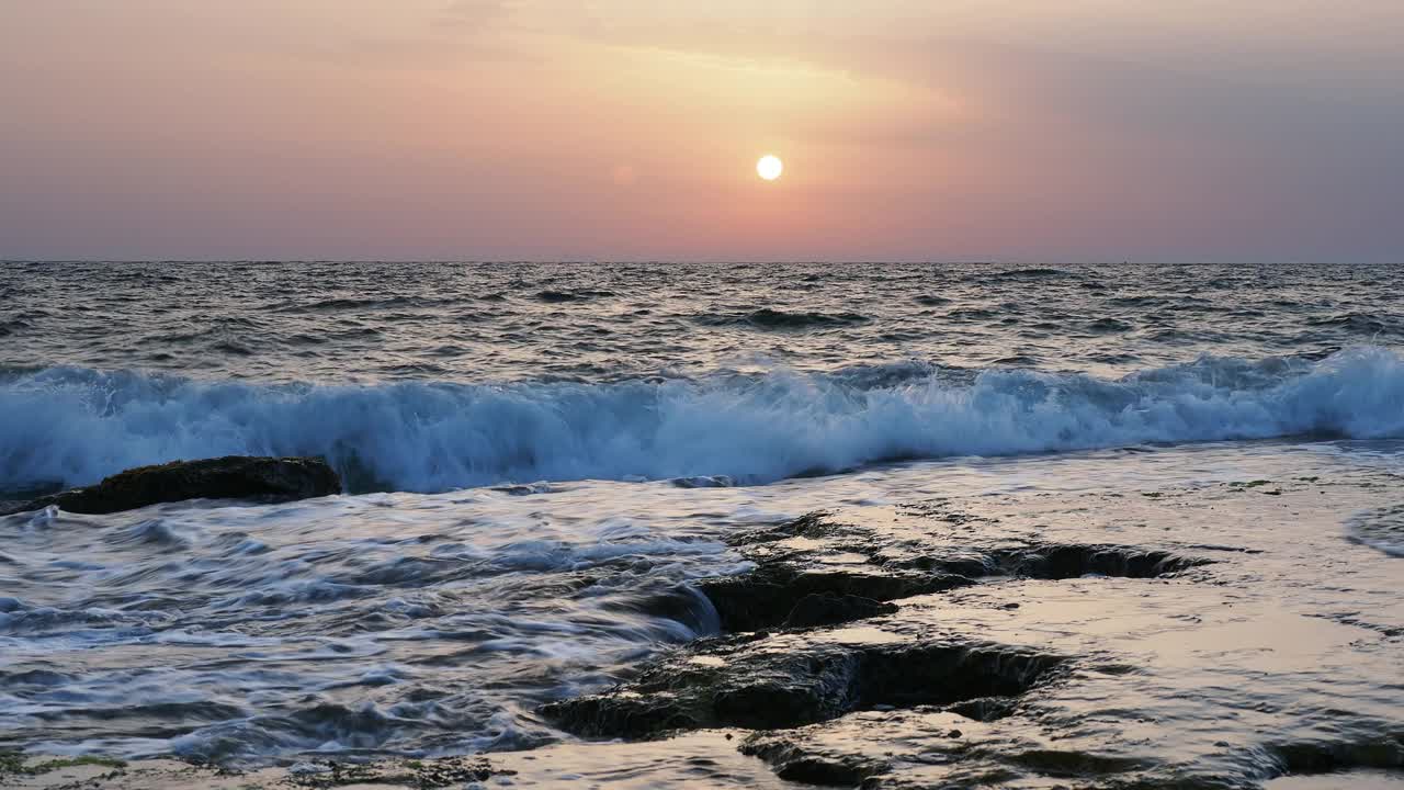 日出时的海岸线景观，太阳在地平线上，海浪拍打着海岸。视频素材