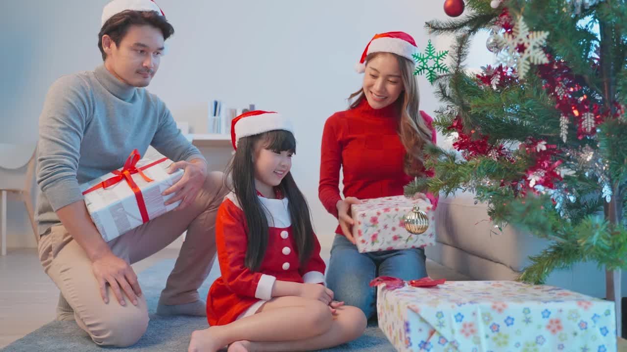 亚洲可爱的家庭成员用礼物装饰圣诞树。年幼的女儿心情愉快，兴奋地和父母一起在家里庆祝节日圣诞节感恩节聚会。视频素材