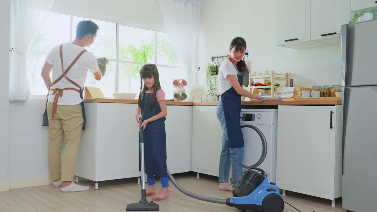 亚洲漂亮的父母教年轻的女孩打扫家里的厨房。可爱的爸爸妈妈帮助和支持小女儿在家打扫房间的地板。活动关系的概念。视频素材