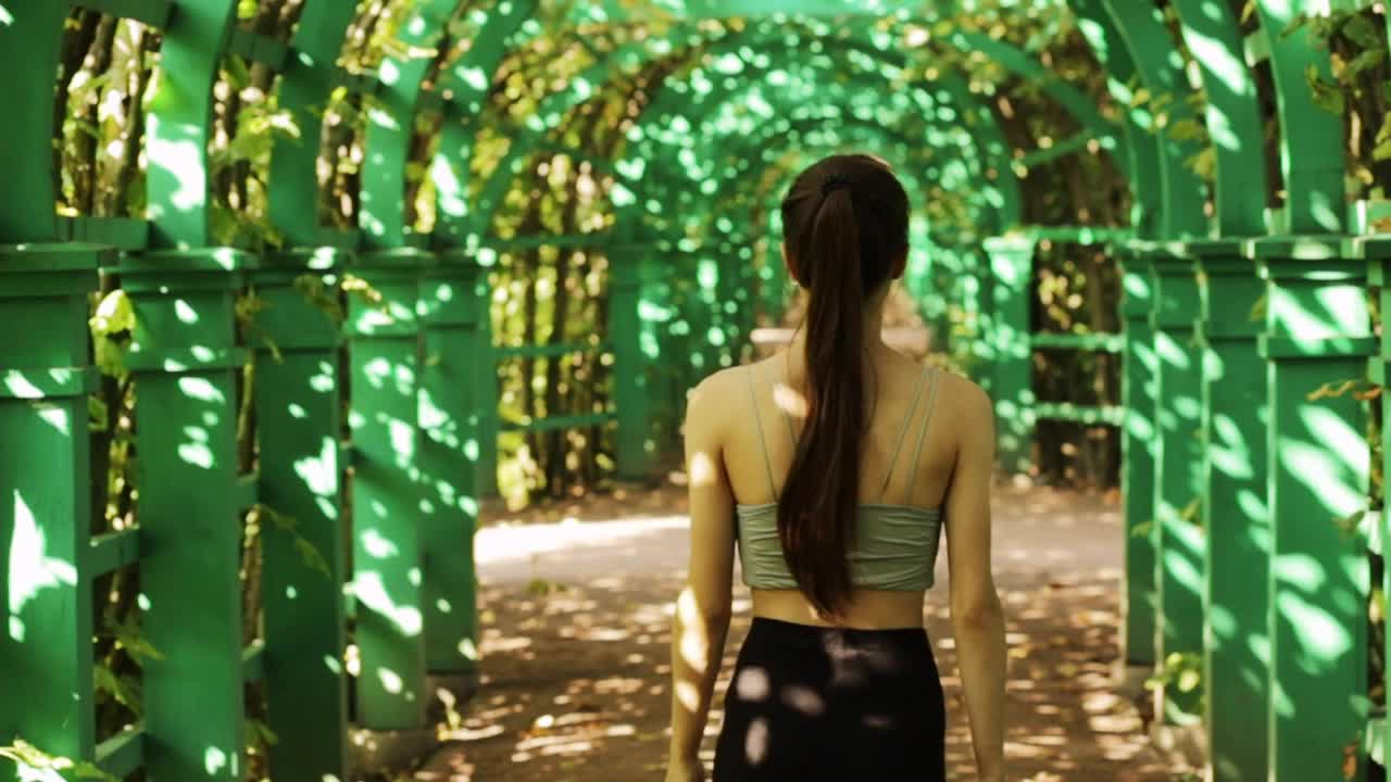 十几岁的女孩在公园里，从后面可以看到一个绿色的夏季拱形树视频下载