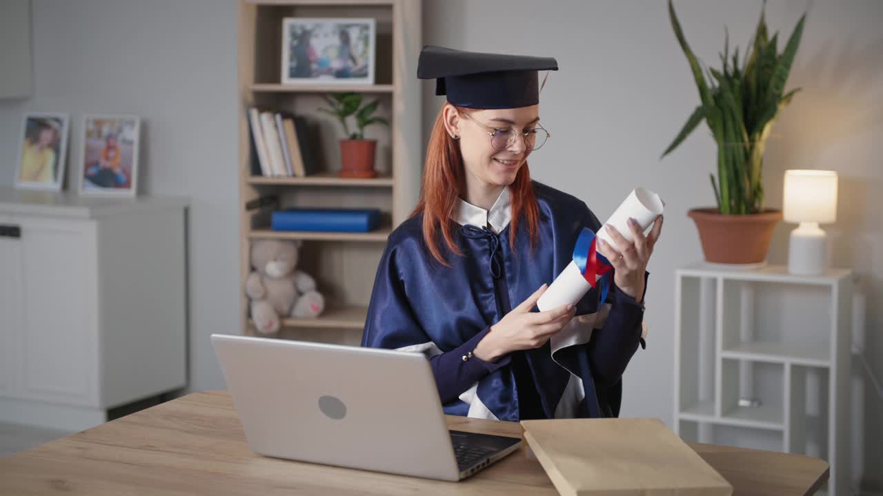 E-learning，一名手持毕业证书的女毕业生坐在家里的气球背景上，用笔记本电脑上的网络摄像头庆祝网上大学毕业典礼视频下载