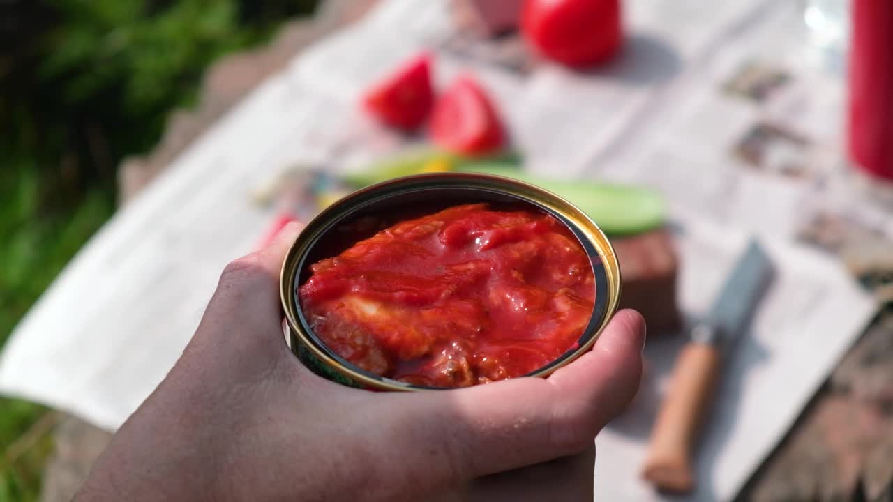一个人拿着叉子拿出番茄酱鱼罐头吃。户外野餐。视频下载