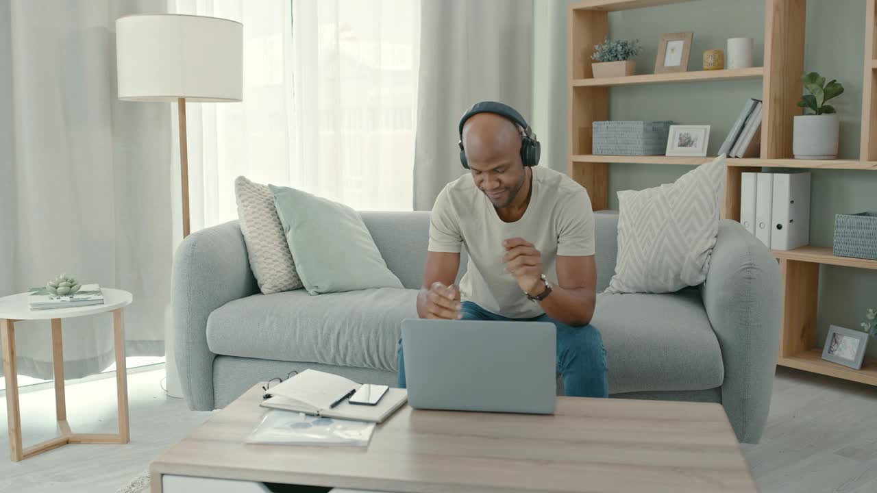 一名男子戴着耳机坐在家里用笔记本电脑跳舞的4k视频片段视频素材