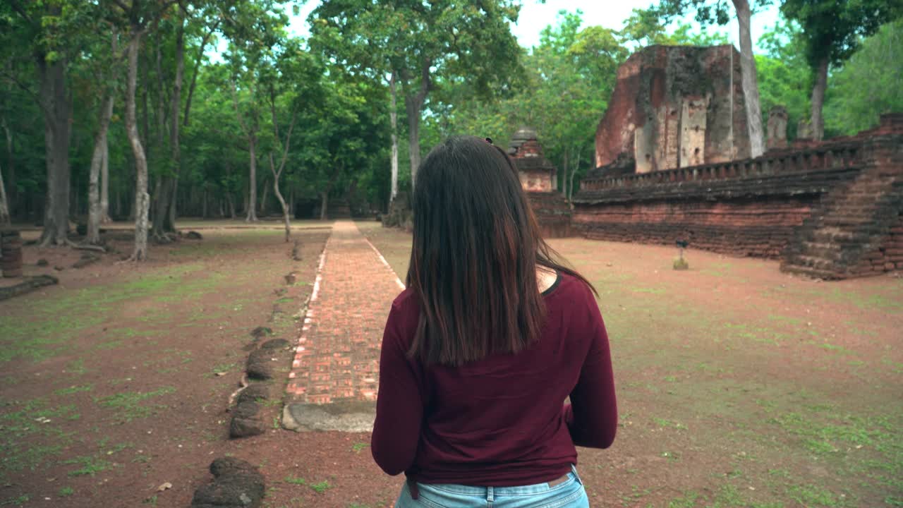 年轻的泰国女子带着纸地图探索历史时刻，在著名的古代甘榜佛寺，后视图视频素材
