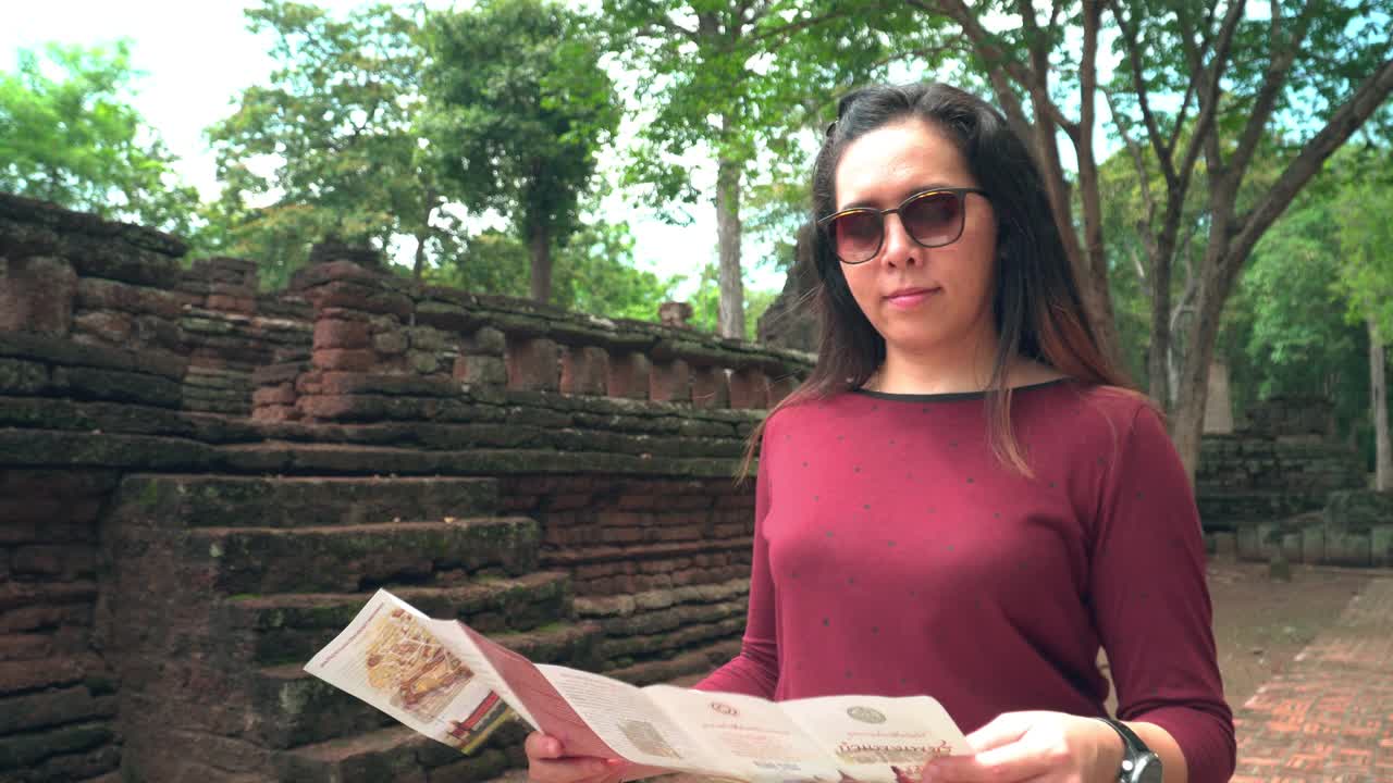 年轻的泰国女子带着纸地图探索历史时刻在著名的古老甘榜Phet寺庙，前面跟随视图视频素材