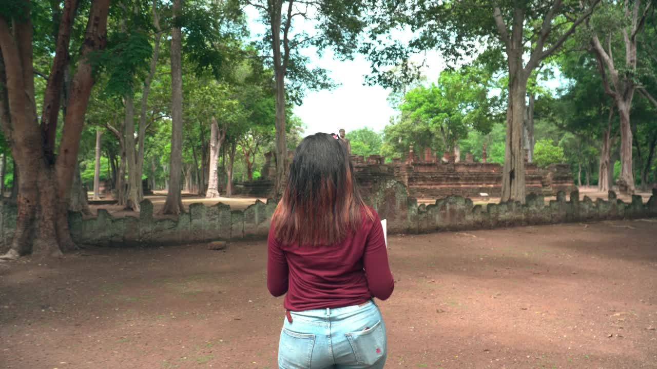年轻的泰国女子带着纸地图直朝方向走，探索历史时刻，在著名的古代甘蓬寺瞻仰古代佛像视频素材