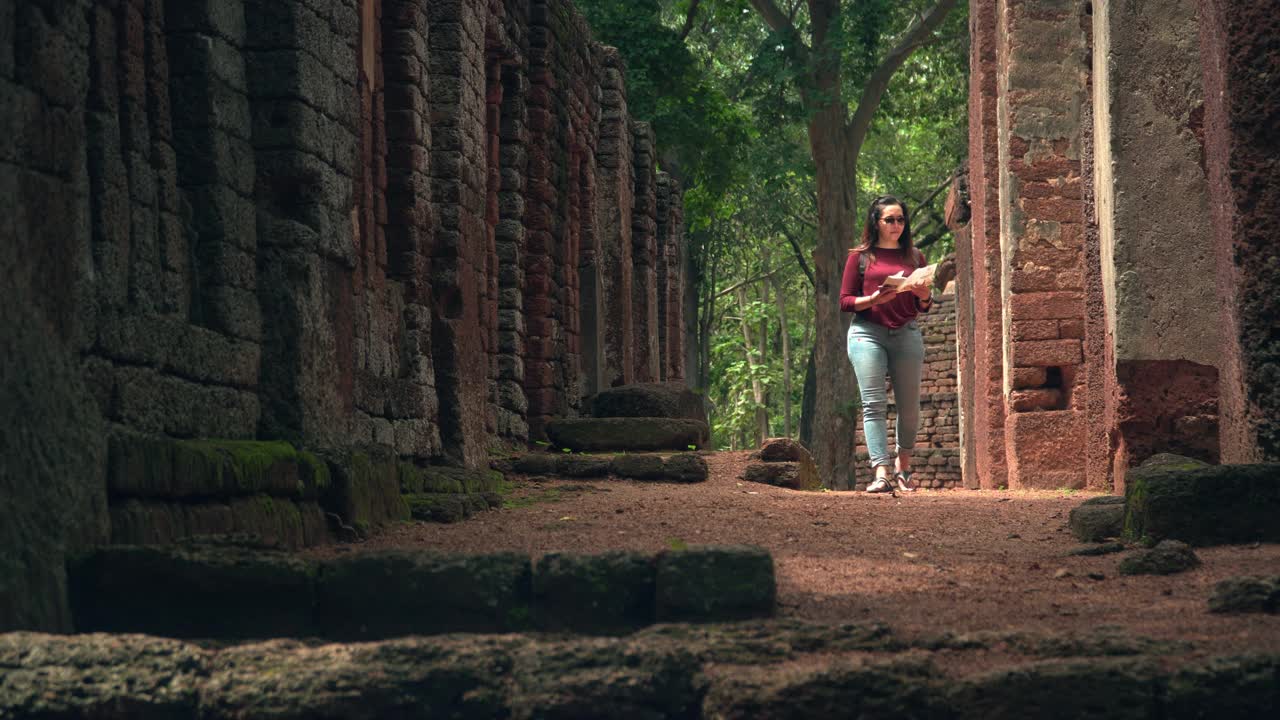一个年轻的泰国女人带着一个小袋子，带着一张纸地图，沿着著名的古老的甘潘寺的砖墙，探索历史时刻视频素材