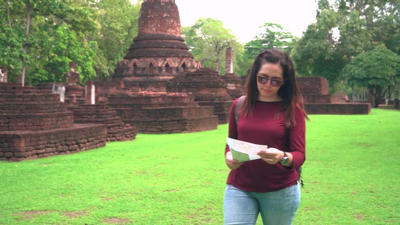 一名年轻的泰国女子带着一个小袋子，带着一张纸地图，在著名的贡彭Phet古庙探索历史宝塔时刻，视频素材