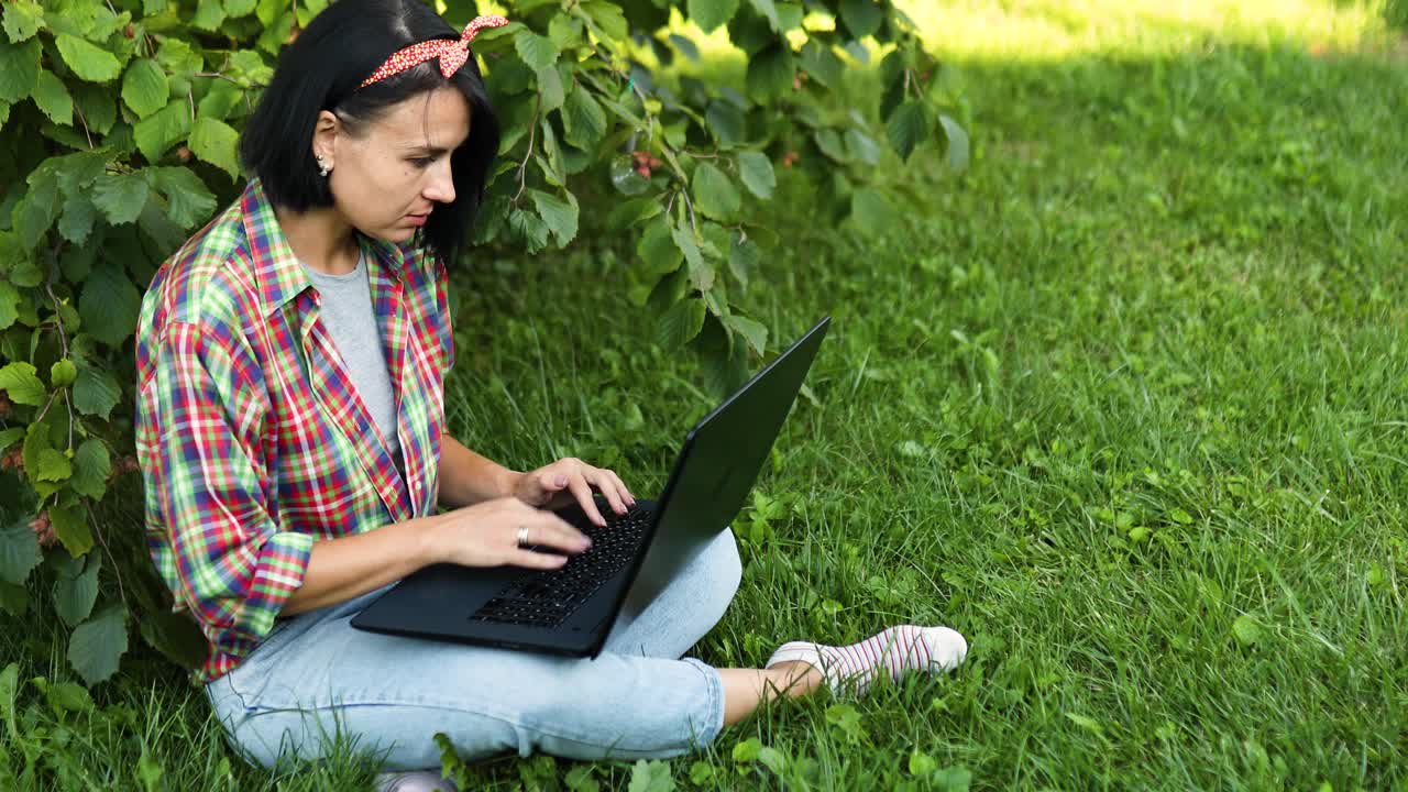 一个穿着休闲装的自由职业者带着她的笔记本电脑坐在公园的草地上视频素材
