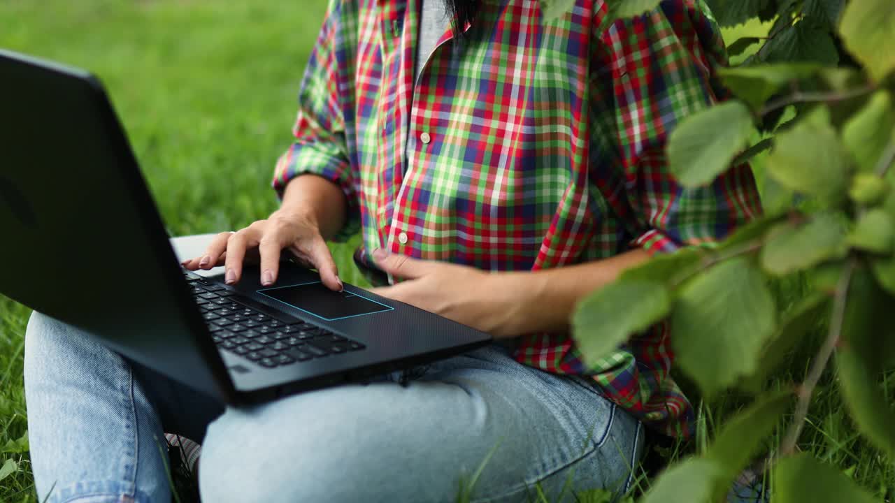 一个穿着休闲装的自由职业者带着她的笔记本电脑坐在公园的草地上视频素材