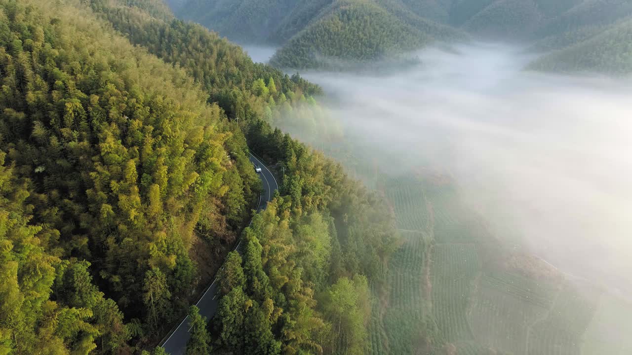 鸟瞰图的汽车行驶在乡村道路与云海起伏的乡村丘陵。视频下载