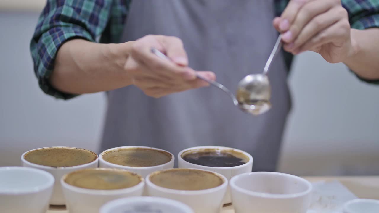 亚洲华人男咖啡师铲咖啡渣，为咖啡杯品尝范围，从桌上的陶瓷杯子上撇去咖啡渣视频下载