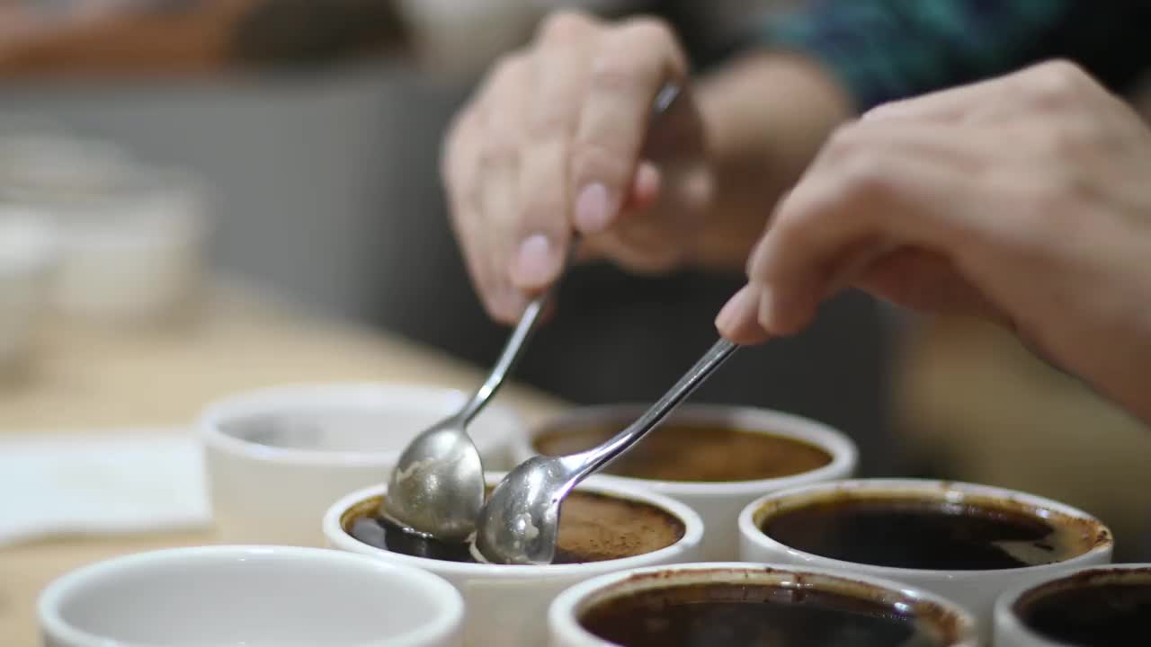 亚洲华人男咖啡师铲咖啡渣，为咖啡杯品尝范围，从桌上的陶瓷杯子上撇去咖啡渣视频下载